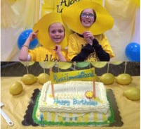 Children with lemon masks standing behind a birthday cake
